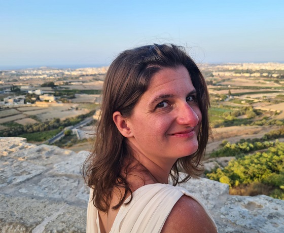 Alison looking behind her shoulder with a countryside landscape in the background