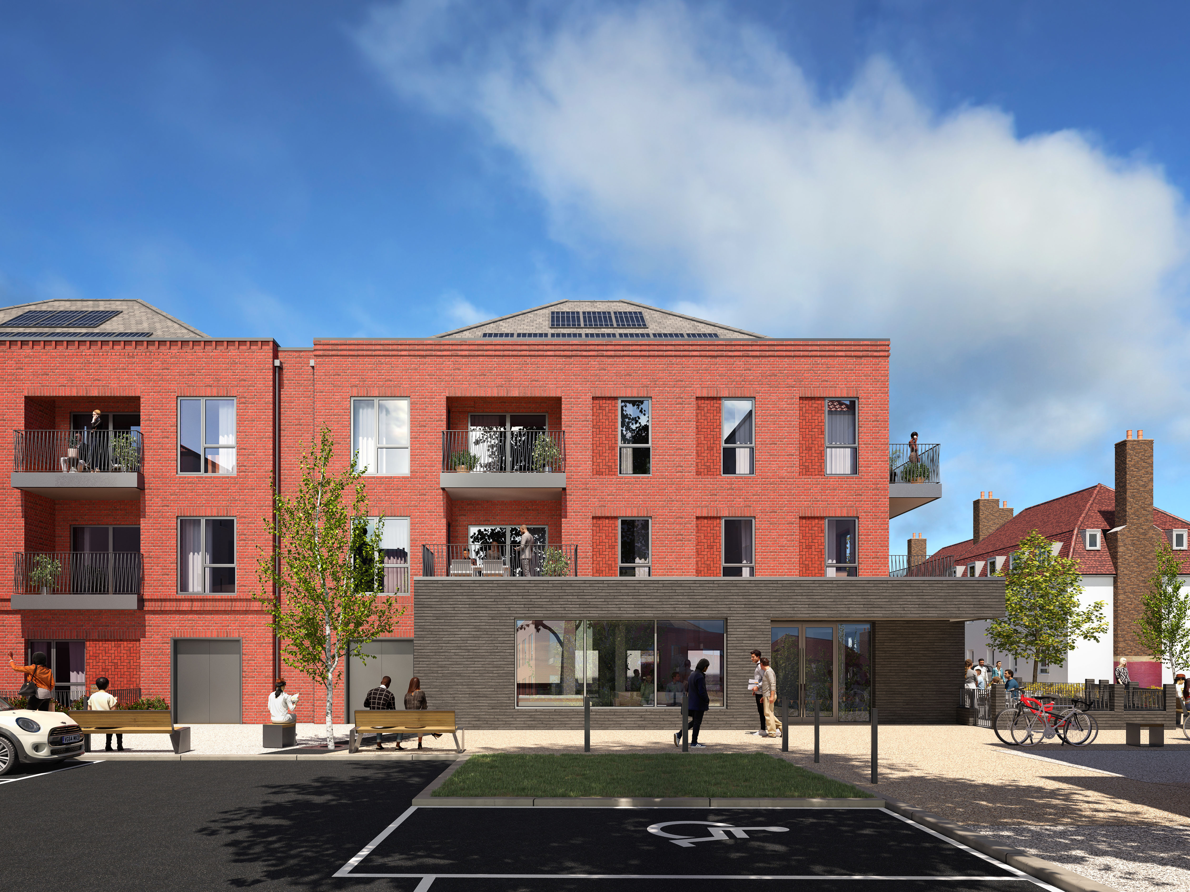 An image showing a block of flats in red brick topped by a slightly sloped roof with solar panels.