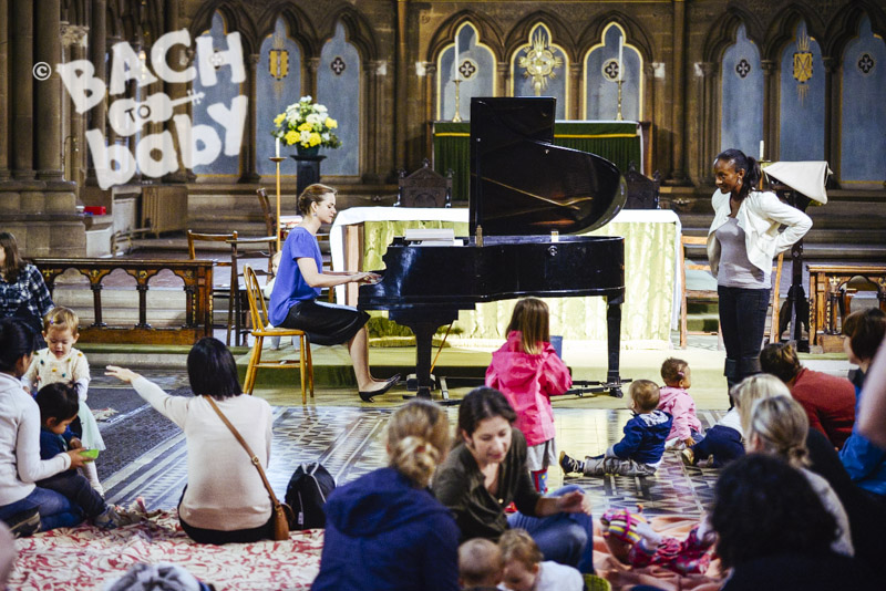 A group of adults and babies watching a pianist perform