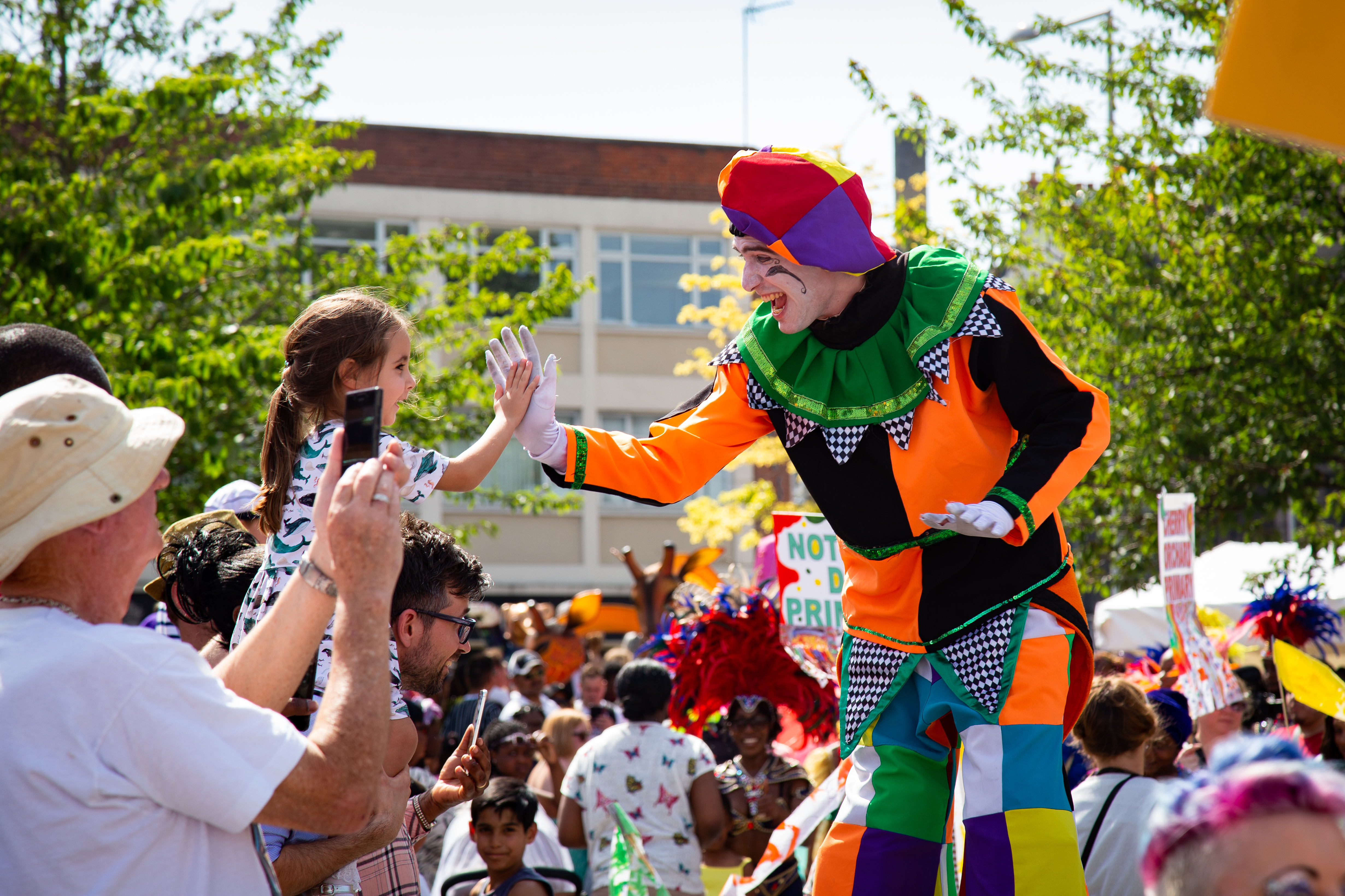 Child and man on stilts high-five on parade