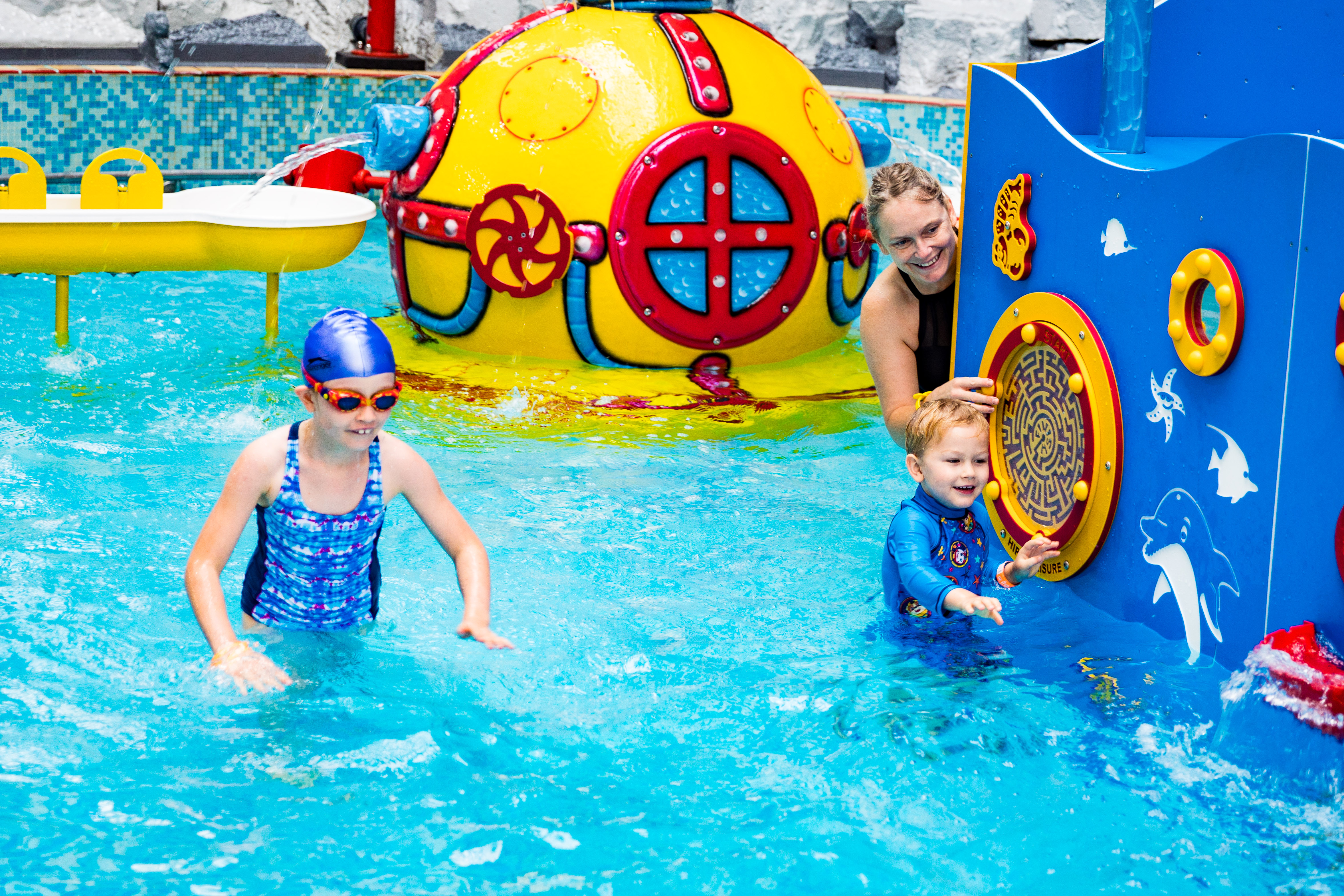 Two children and an adult swimming in the children's leisure pool.