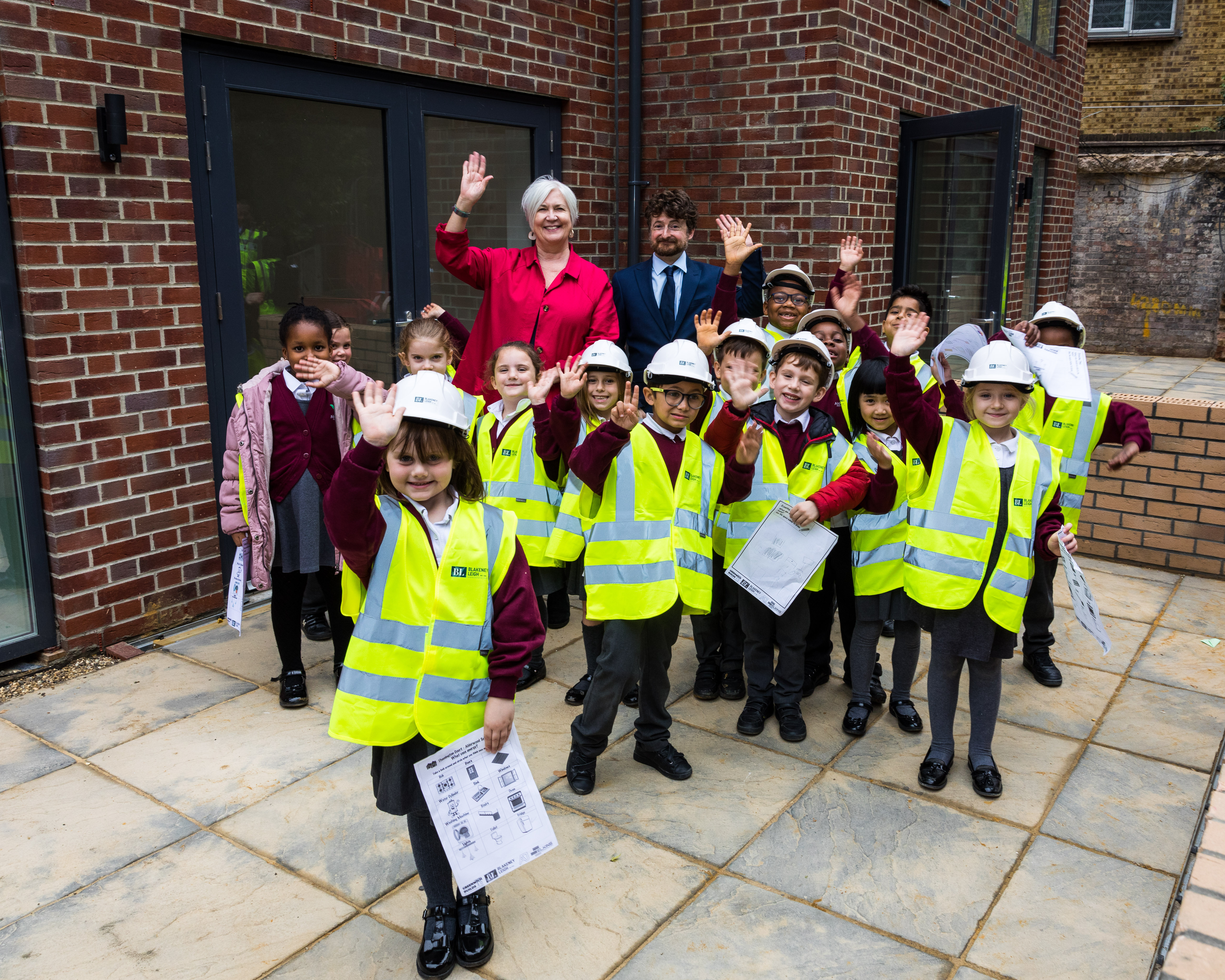 A group of year 2 primary school children in hi-vis vests and hard hats with councillors Aidan Smith and Pat Slattery outside newly built council homes