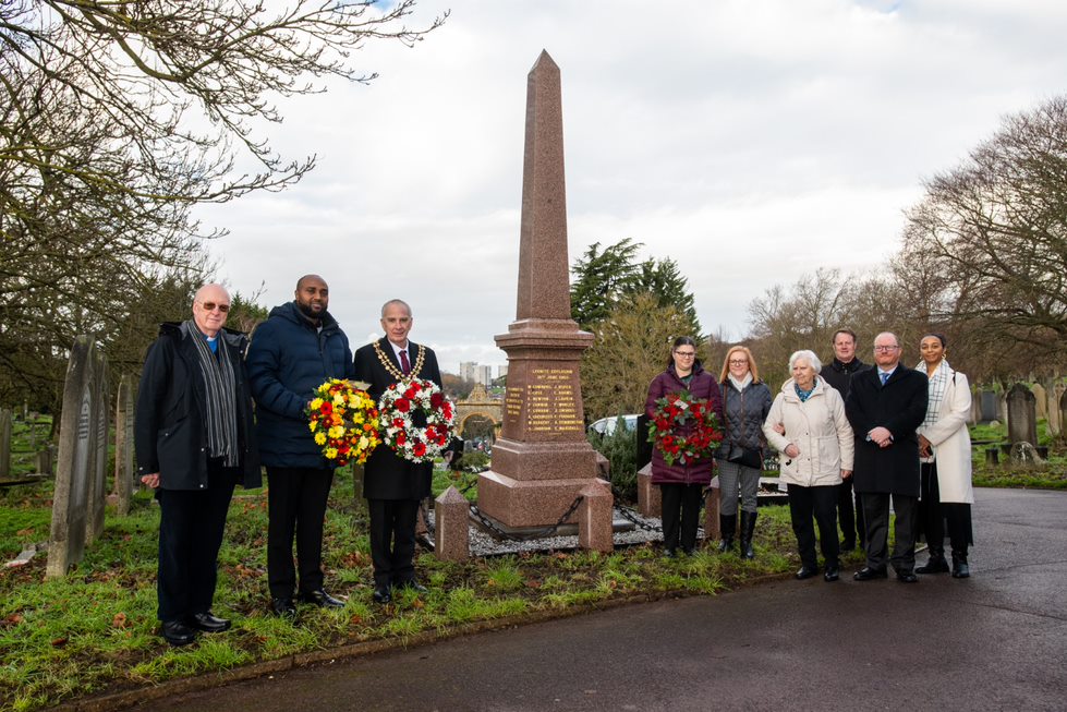 Cllrs Khaireh and Fletcher stand to the left of the Woolwich Arsenal war memorial holding wreaths. To the right a group of people have joined them to support the reopening of the memorial.