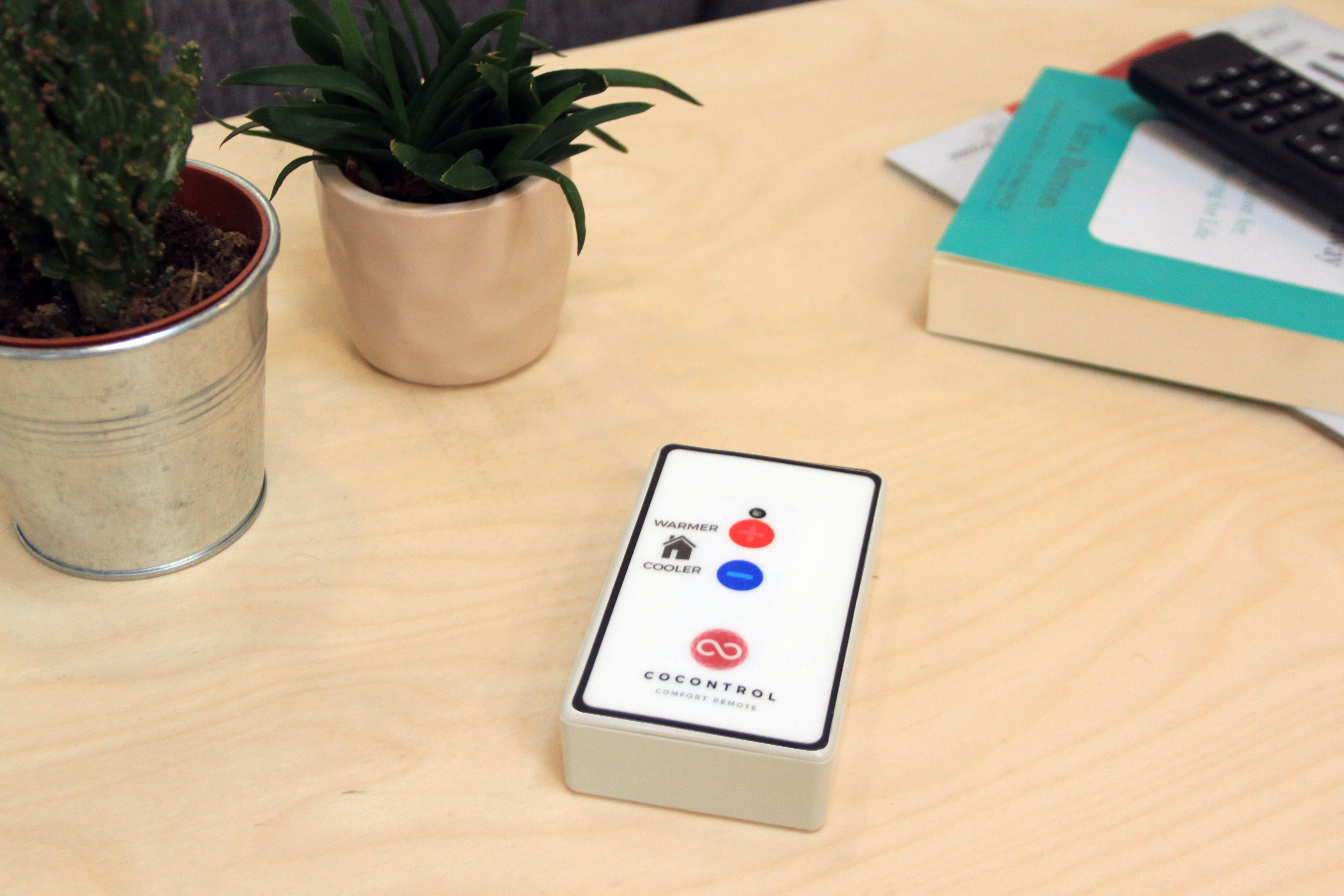 Picture of the smart thermostat remote control on a table, next to two plants.