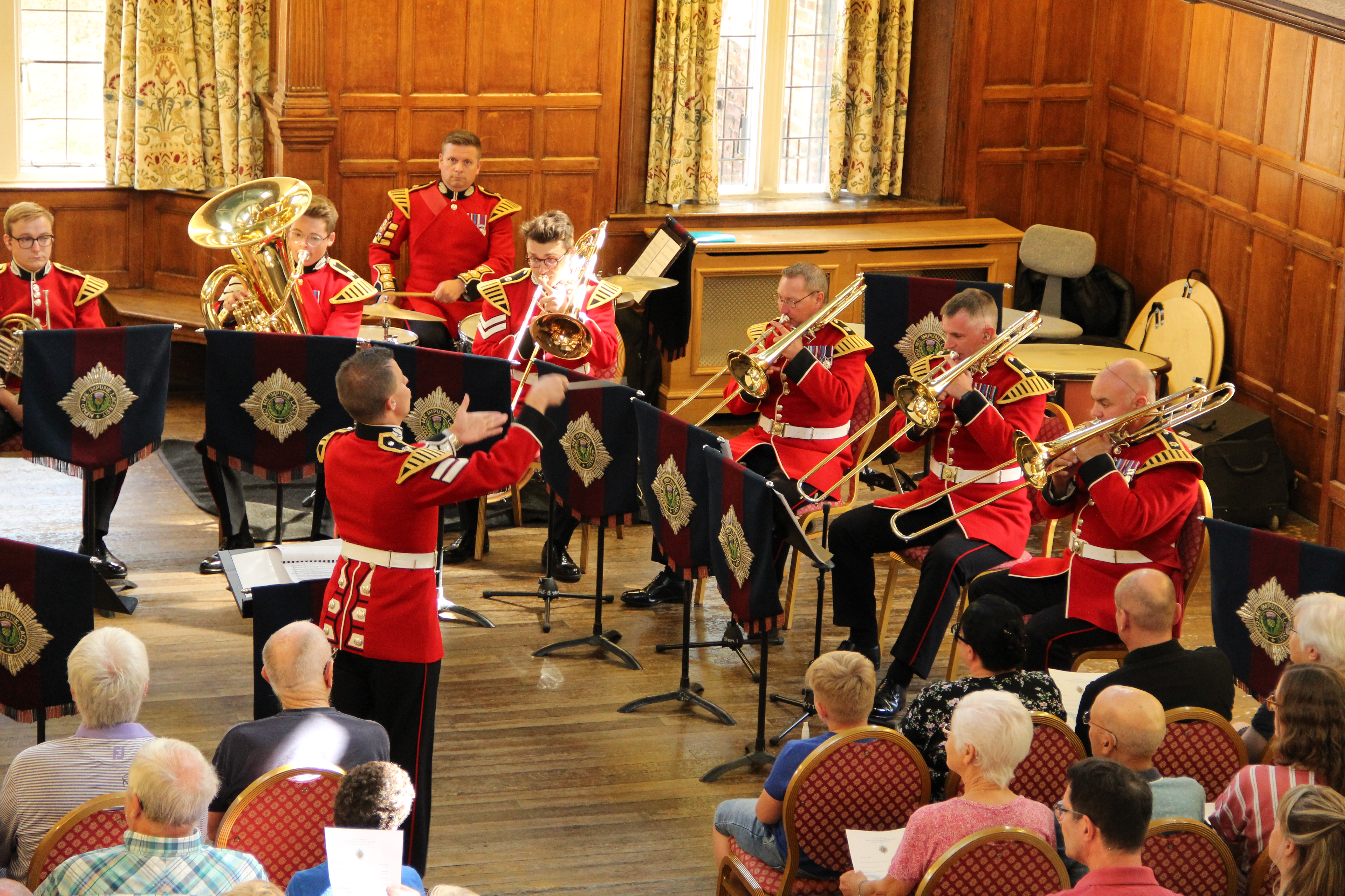Men in red coats playing in a brass band with a conductor