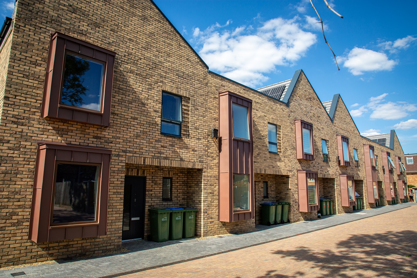 View of the completed homes at Kyle Mews, a row of modern, terraced, two-storey houses in yellow, with protruding window boxes in a bronze colour