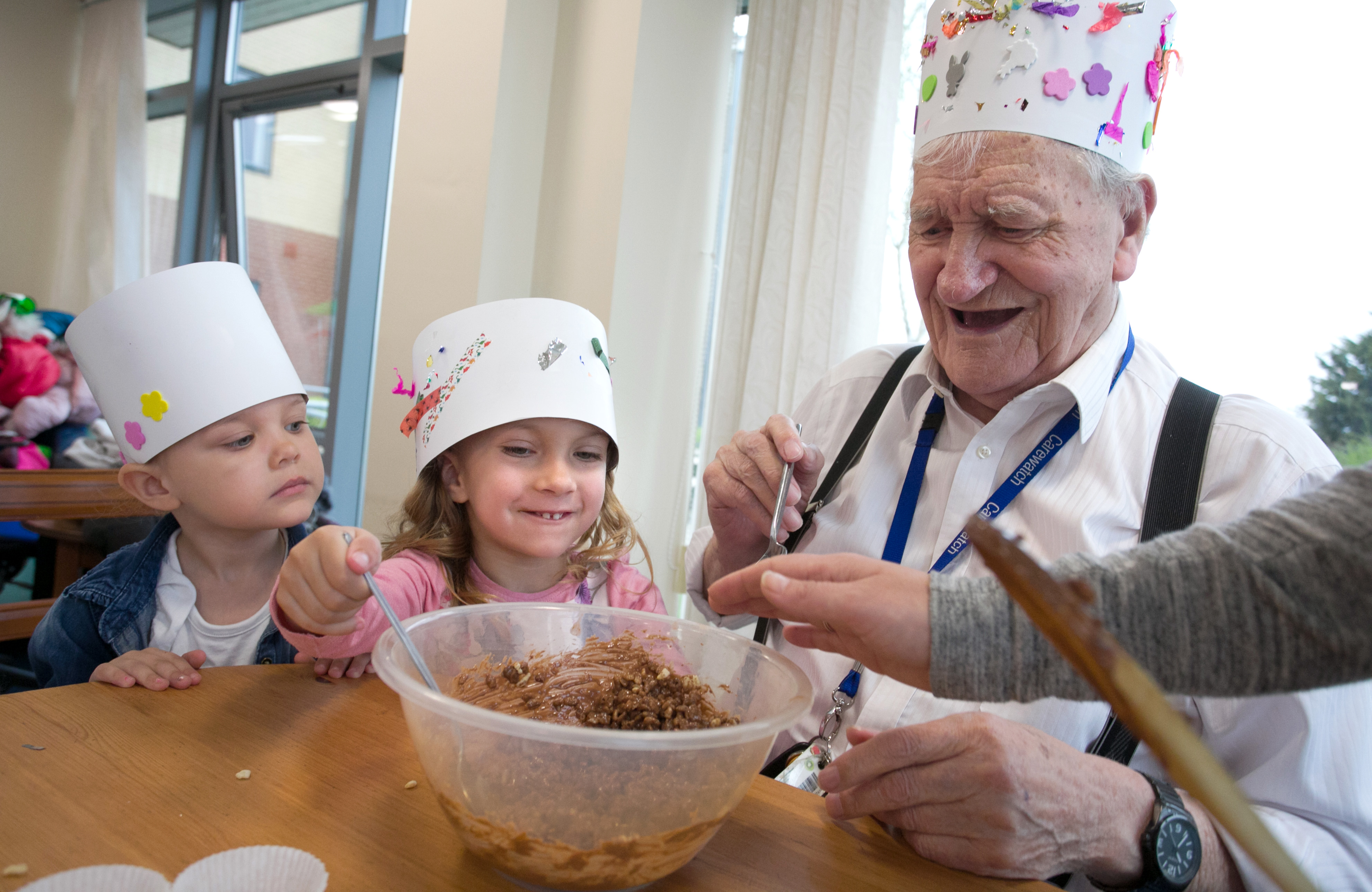 Elderly resident pictures with two nursery children, making Easter treats