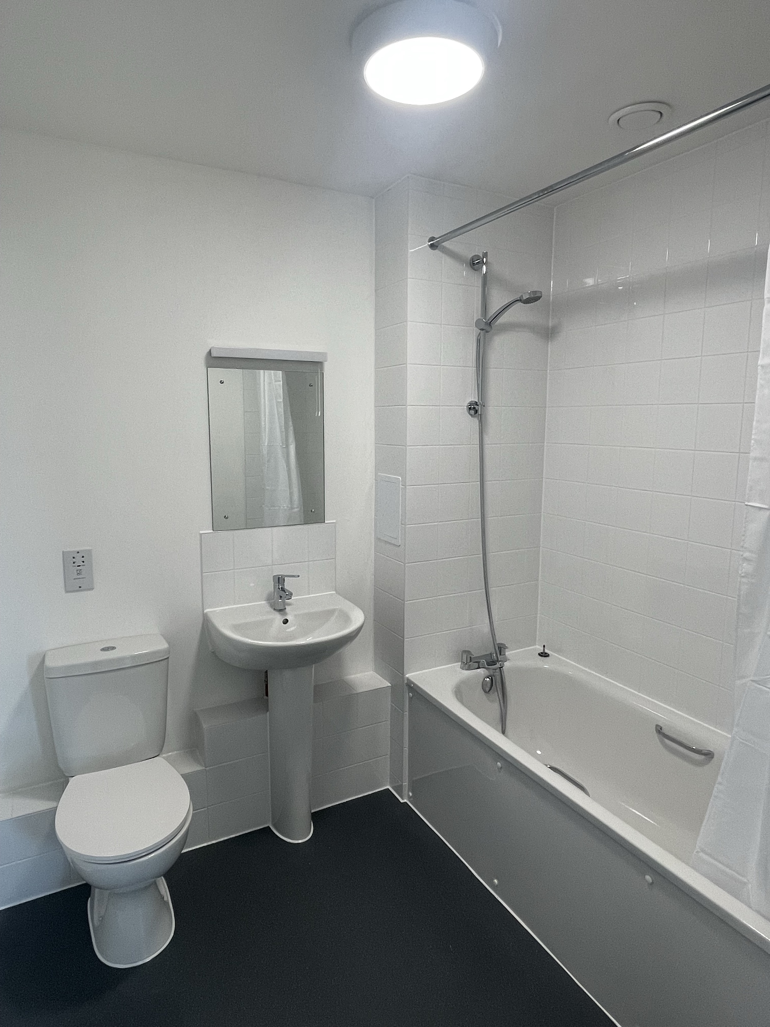 A new bathroom with a toilet, sink and mirror and bathtub.