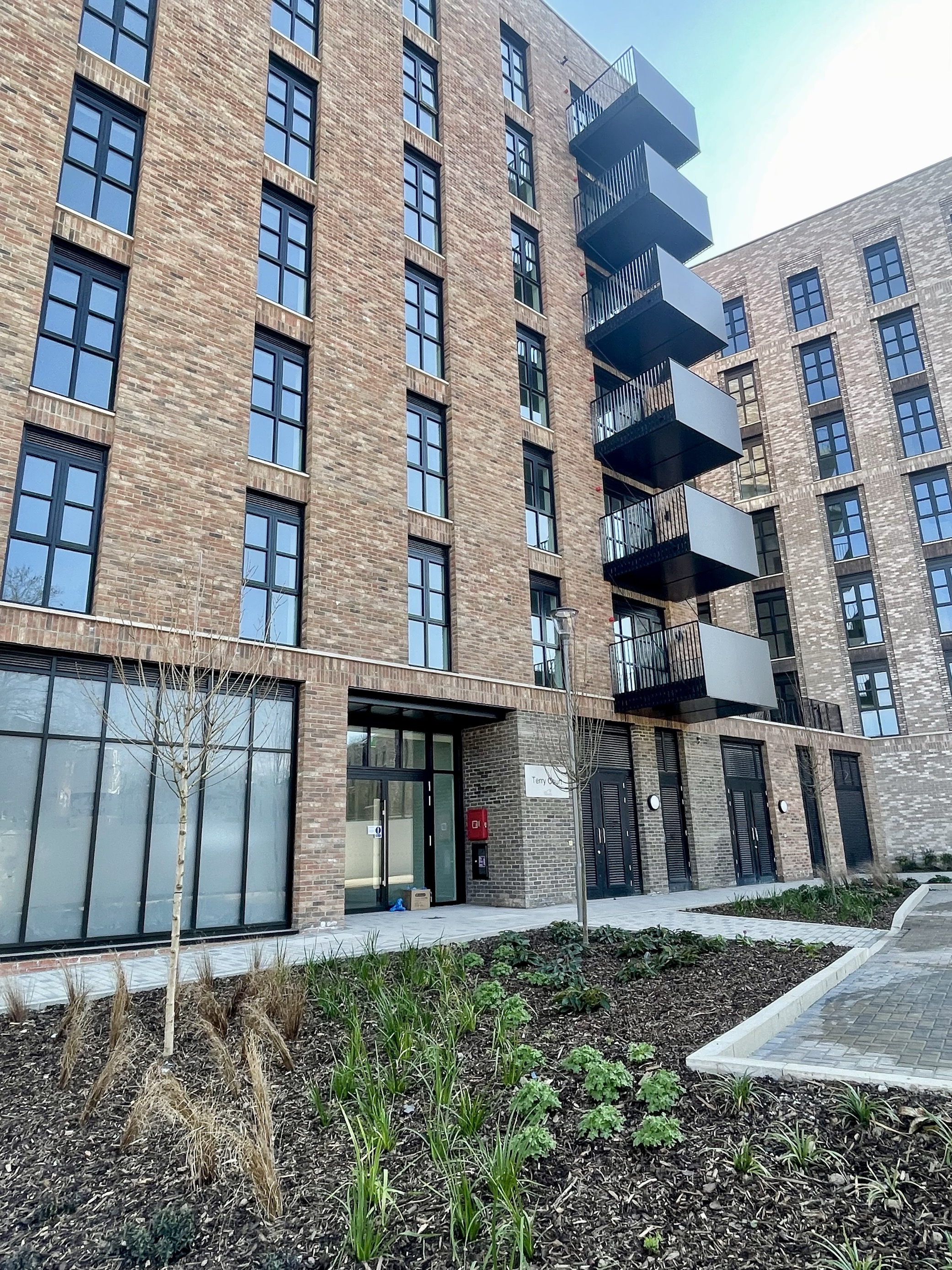 A modern housing block with balconies, beside an outdoor green space and a footpath.