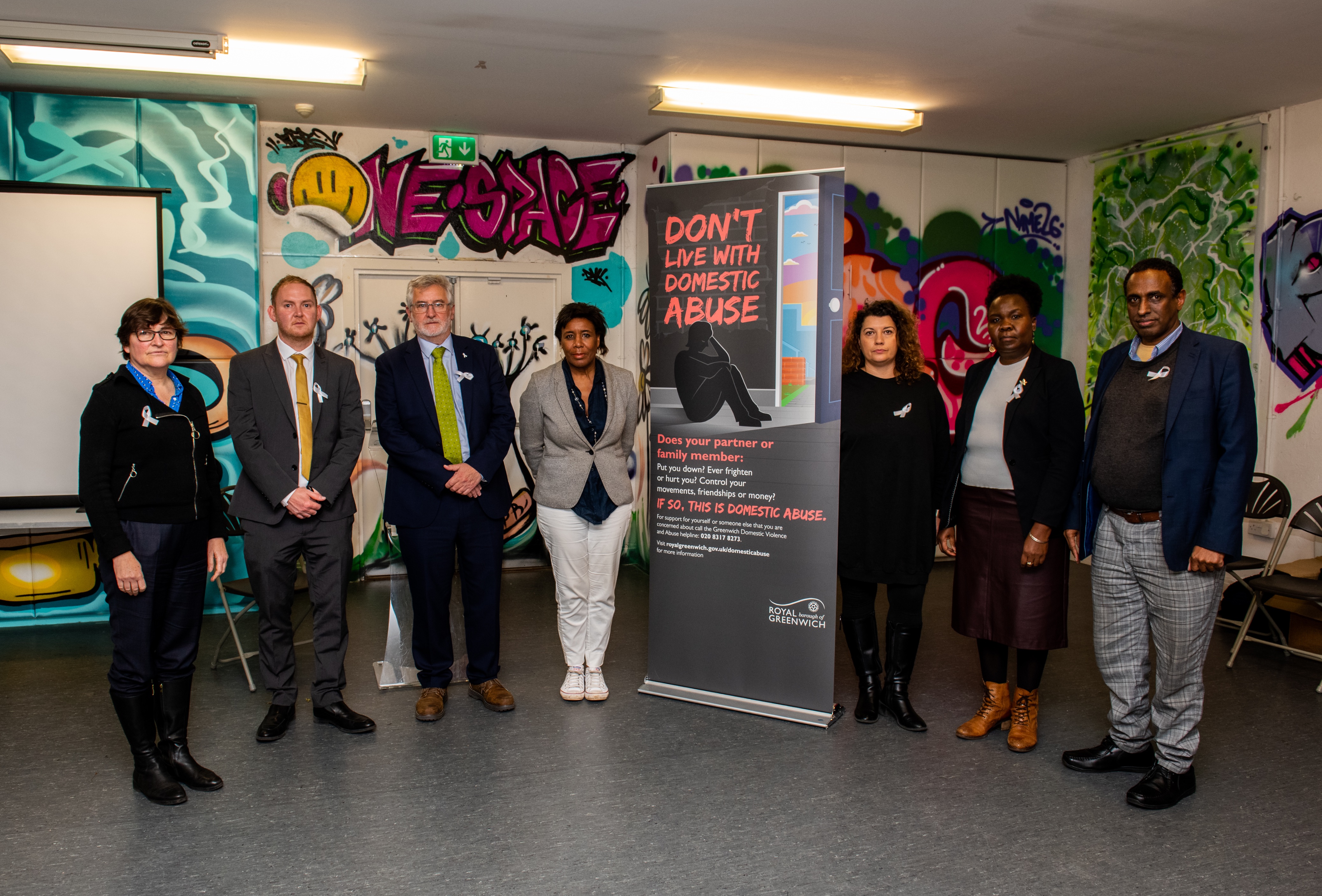 Standing in front of a domestic abuse sign, from left to right are: Stacy Smith, Cllr Danny Thorpe, Clive Efford MP, Cllr Denise Scott-McDonald, Suha Al-Khayyat, Mary Otuko and Adale, male advocate from Forward UK