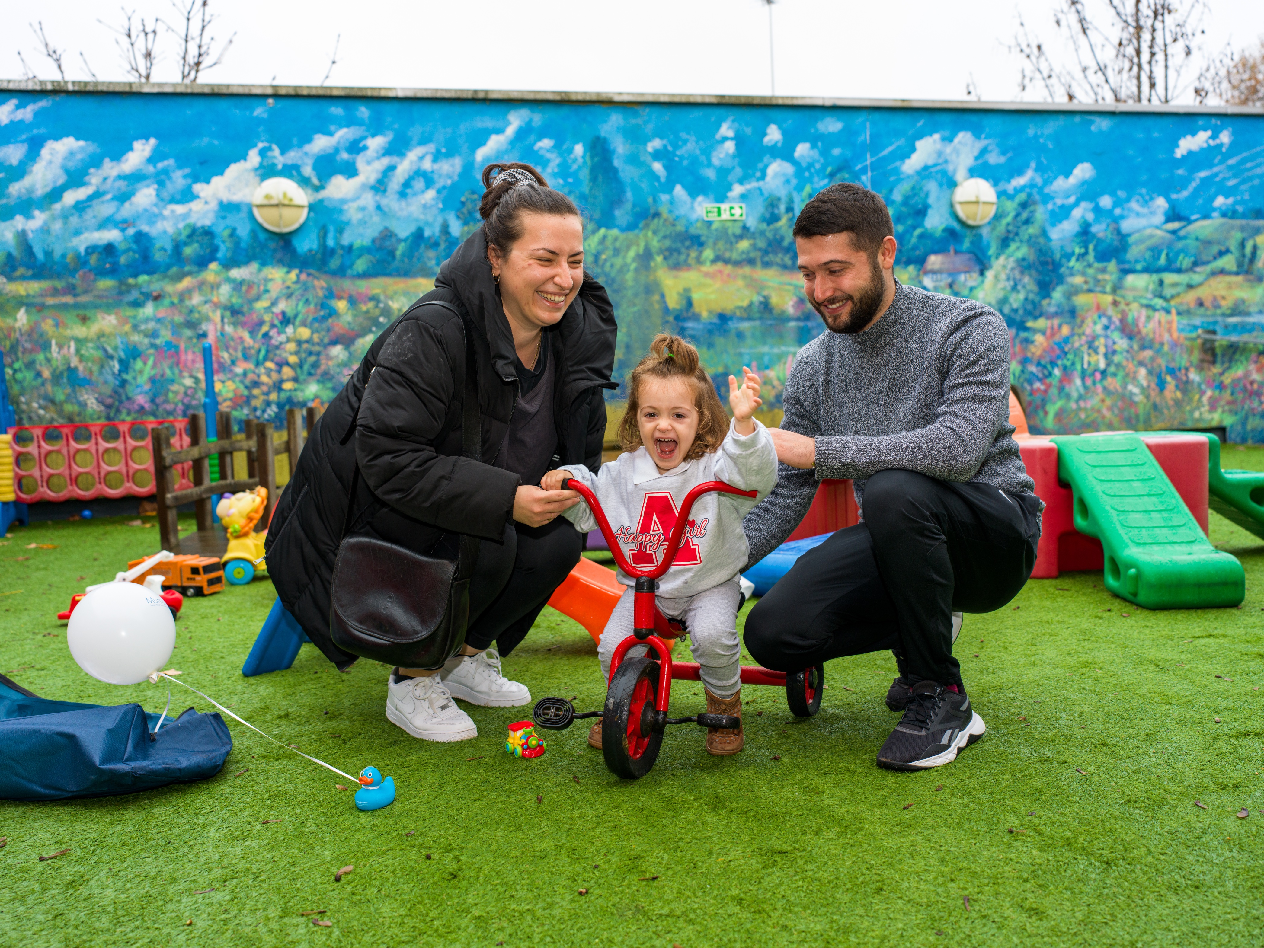 Parents with a little girl playing on a red tricycle