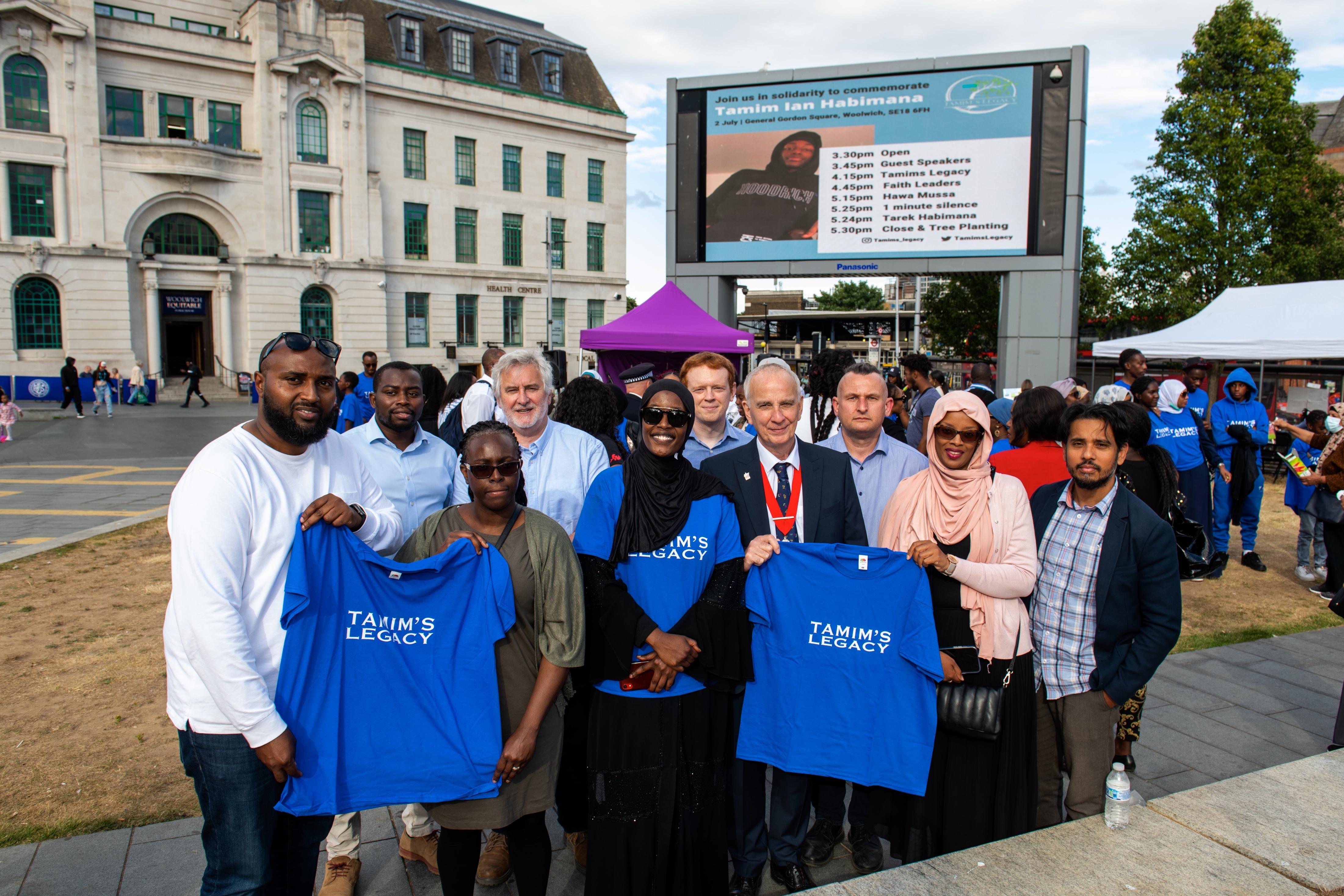 Image shows local councillors from the Royal Borough of Greenwich, with the family of Tamim Ian Habimana, holding t-shirts saying 'Tamim's Legacy' in General Gordon Square, Woolwich