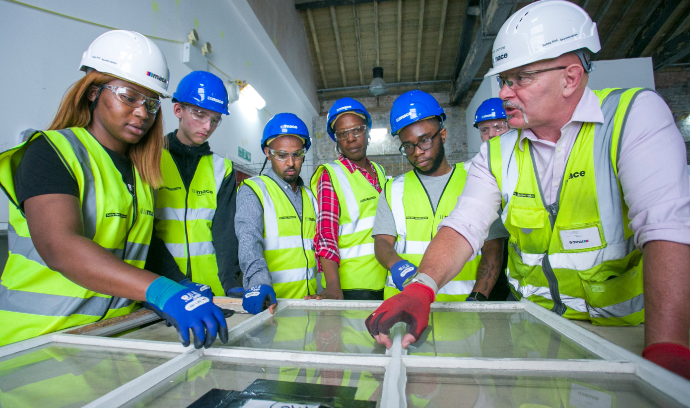 Cohort of past trainees in a workshop wearing hi-vis and helmets