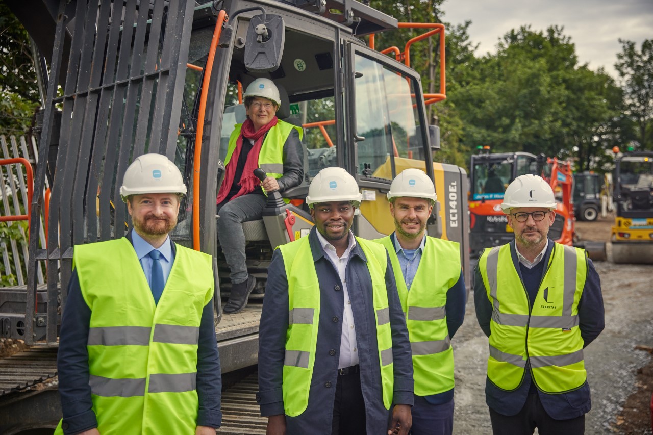 Councillor Aidan Smith, Councillor Jo Van den Broek, Leader of the Council Councillor Anthony Okereke, and members of the Pocket Living development team in high-visibility jackets in front of a digger at the Heights building site.