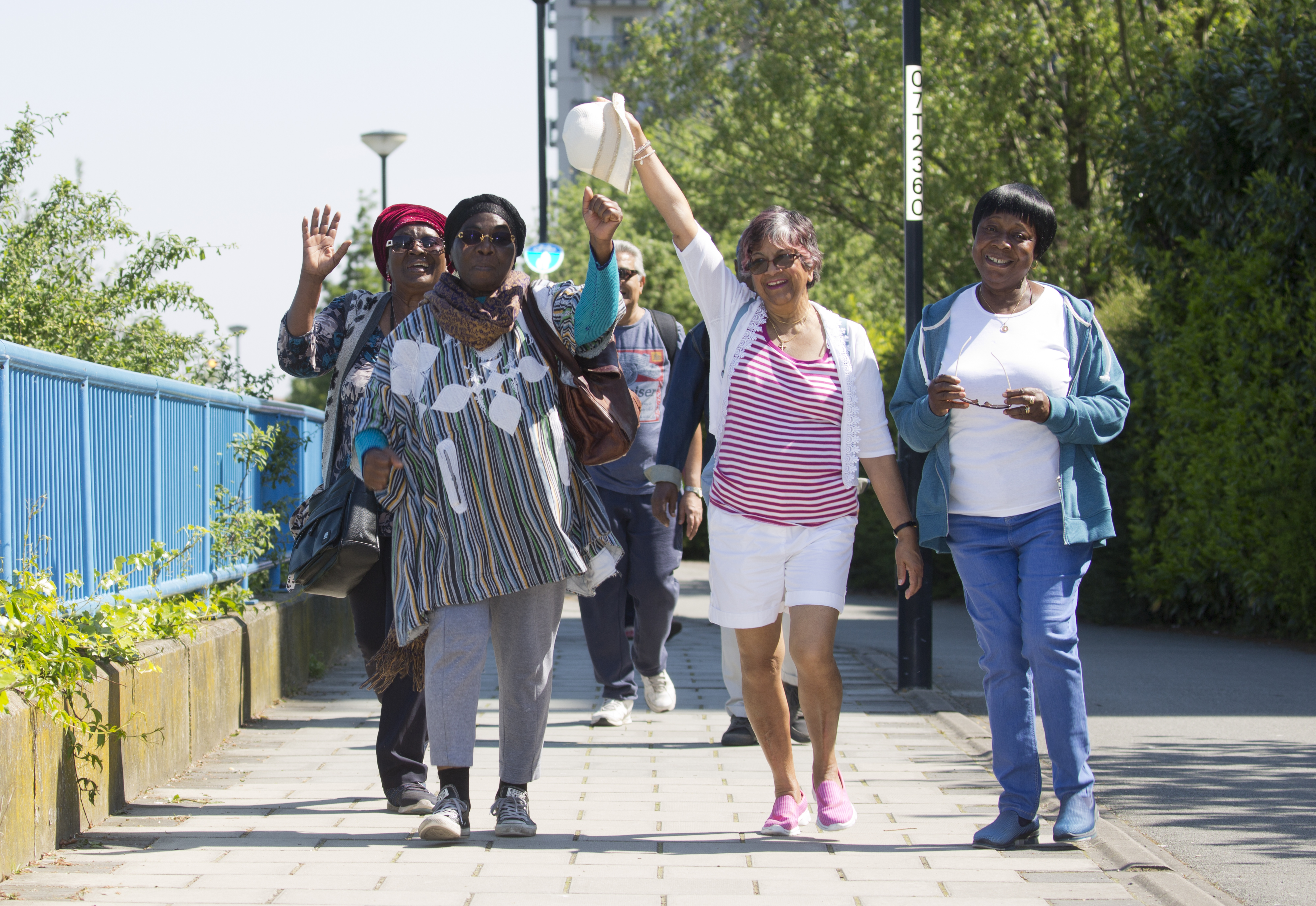 A group of people participating in a walking group, three women have their hands in the air smiling.