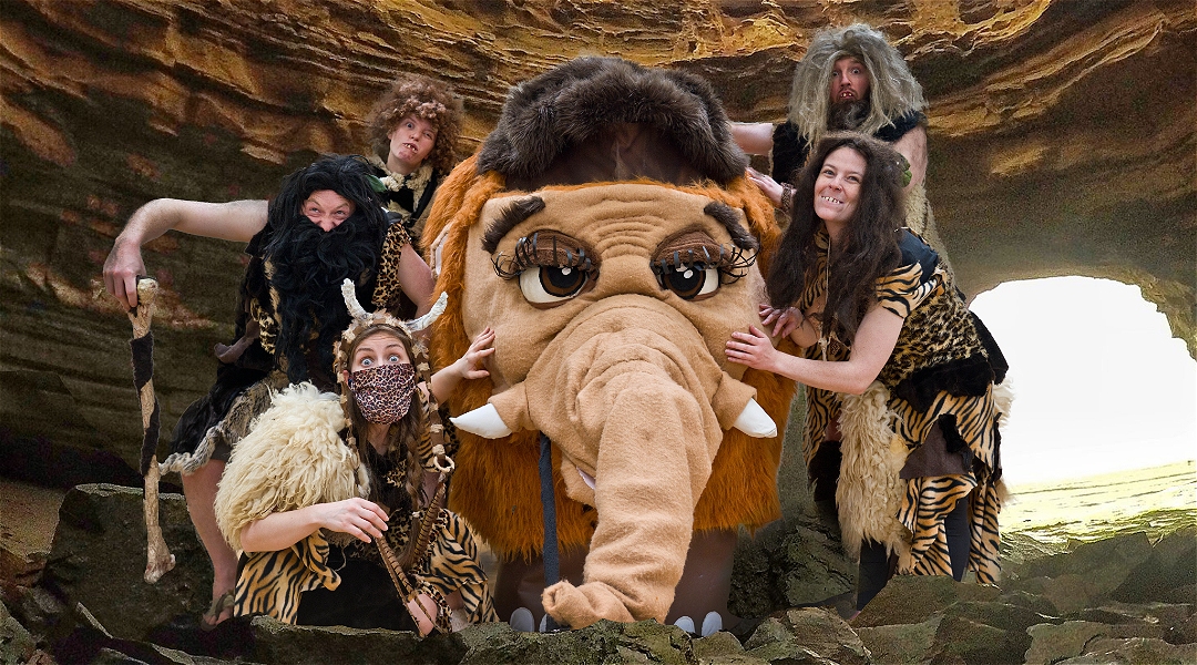 People dressed up as cavemen with a large wooly mammoth