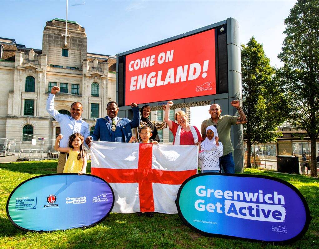 Cllrs Ranabhat. Mbang, van den Broek and Mohammed and some children cheer, while holding an England flag. The screen behind reads 'Come on England!'