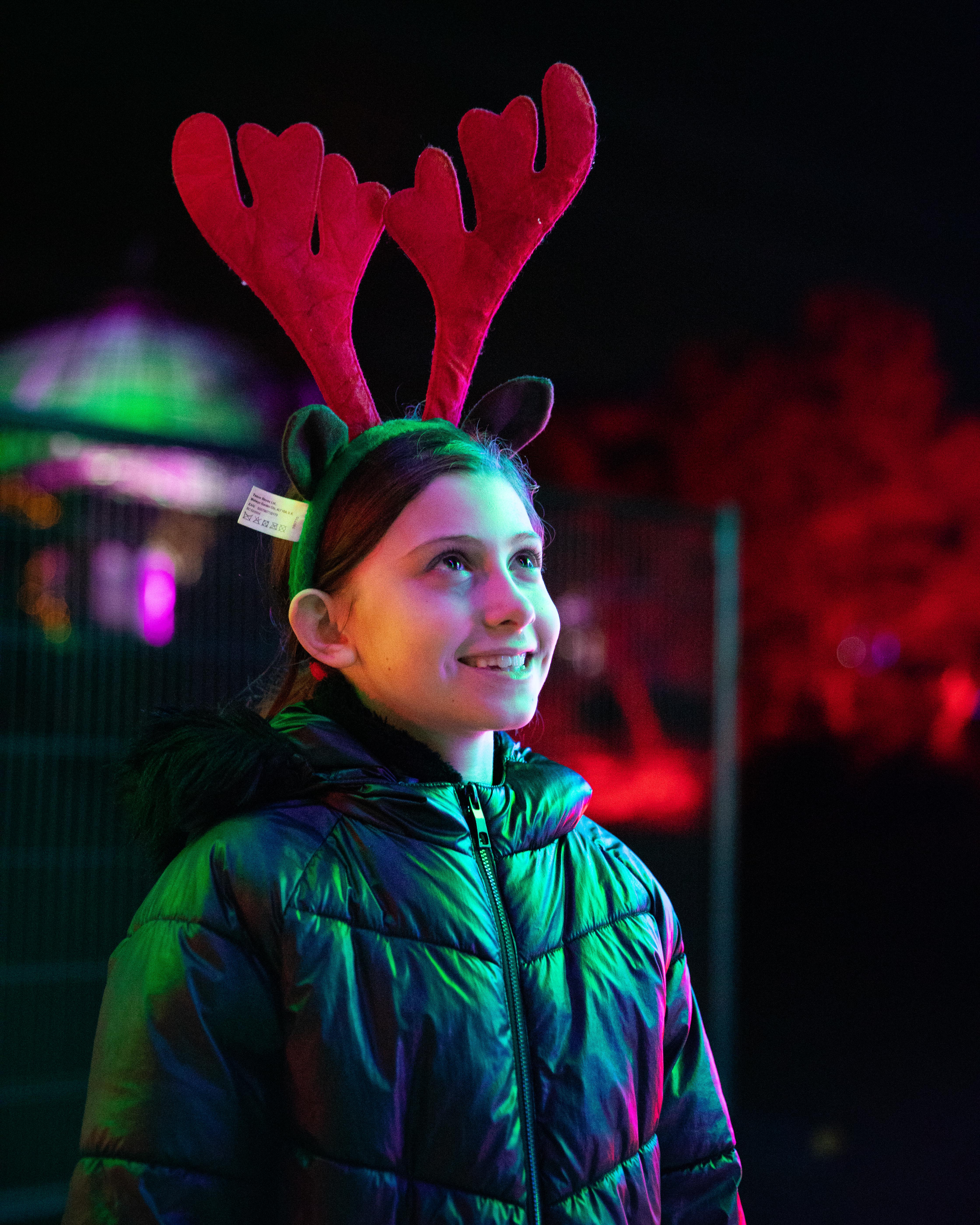 Young girl in red reindeer ears looking at lights at night at the Sparkle in the Park event 2021