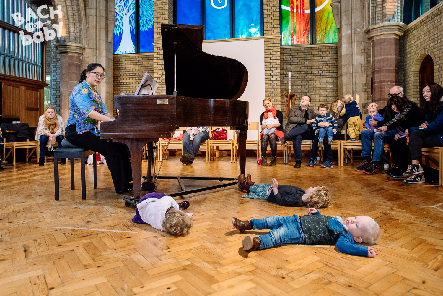 A group of adults and babies watching a pianist perform