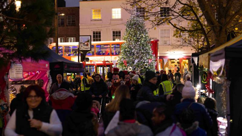 A town centre Christmas market at night with a Christmas tree and a crowd of people.