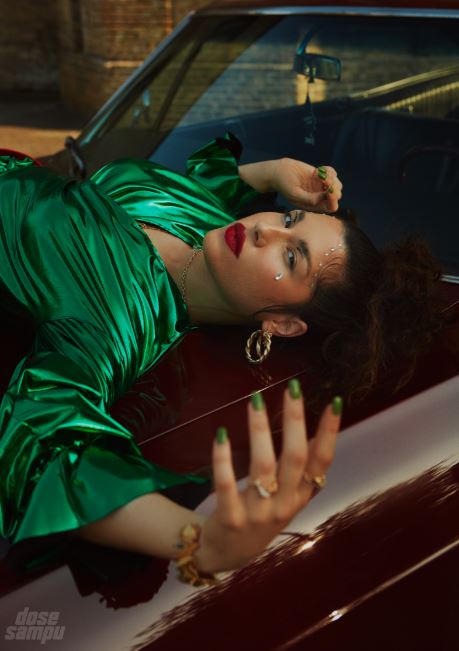 Desta French. Female singer in a green outfit and red lipstick. Laying on a car looking at camera. 