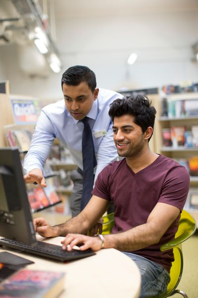 Man helping customer on computer at library.