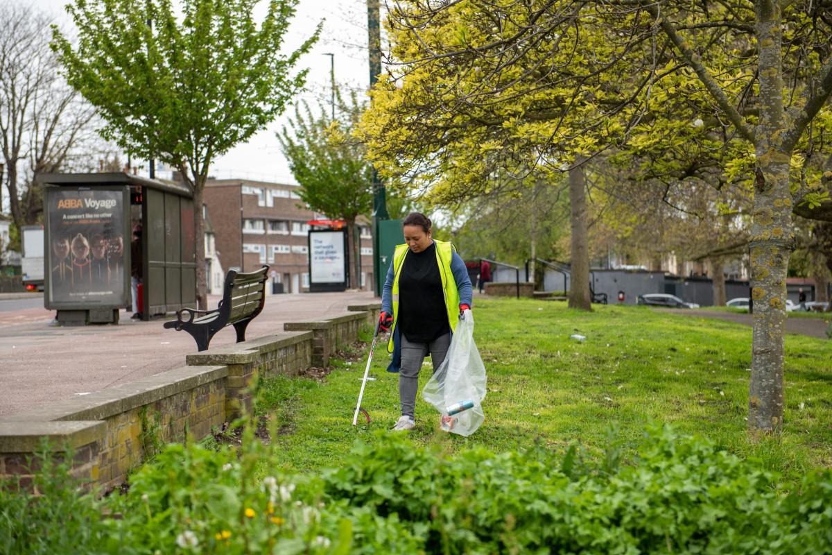 A photo of a woman picking litter from the grass with a hi-vis jacket on.