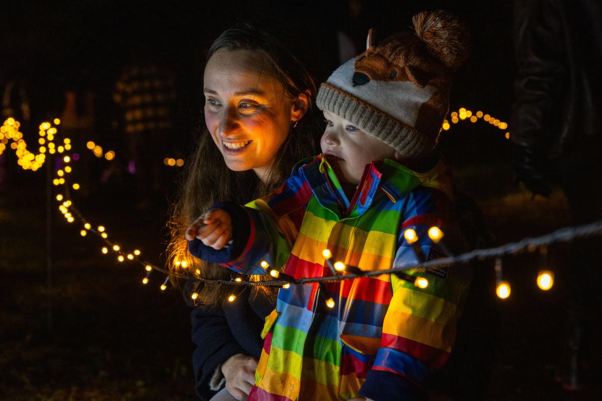 A woman and a young child dressed in a rainbow coloured jacket look at fairy lights