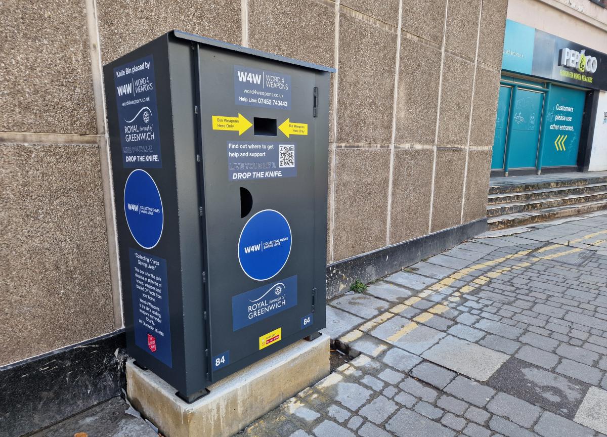 A photo of the knife amnesty bin in Woolwich Town Centre. A grey metal bin installed on a concrete base.