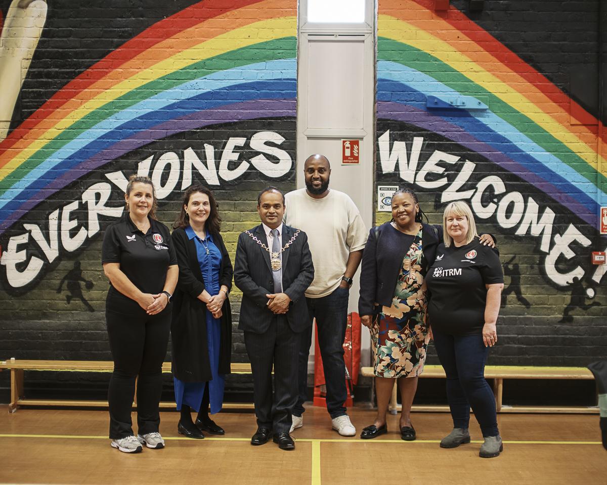 A group photo of youth hub staff and councillors standing in front of a painted mural wall which says 'everyones welcome'