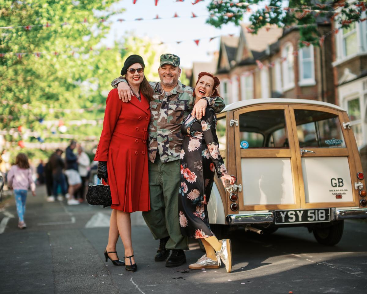 Three people in 40s clothing standing next to a vintage car
