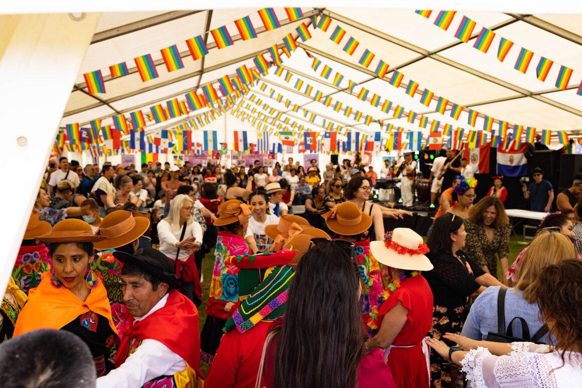 A group of people in a white marquee tent decorated with pride flag rainbow bunting