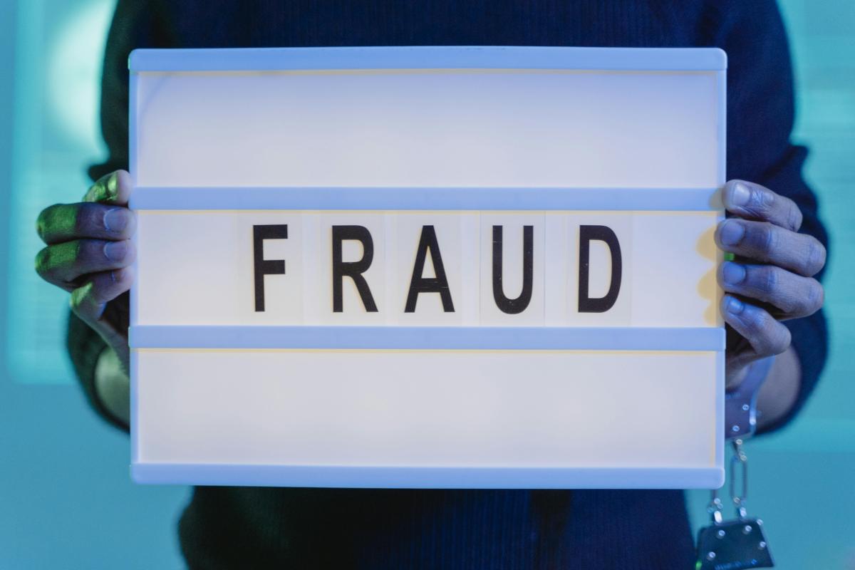 Image of a person holding a sign that reads 'FRAUD'