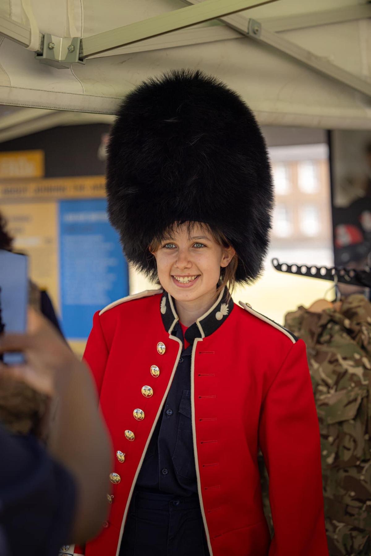 A person wearing a traditional red soldier jacket and black 'bearskin' hat