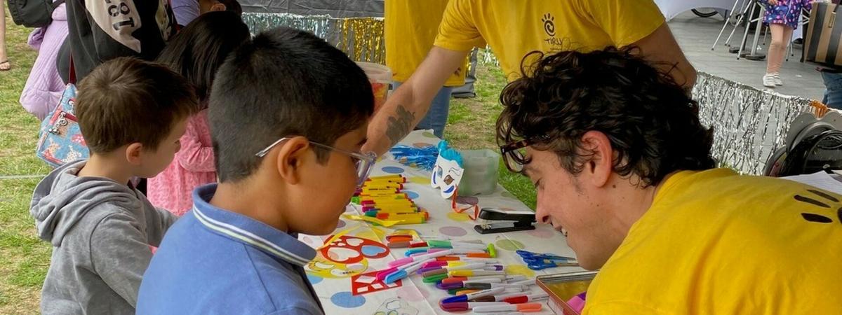 A group of adults in yellow tops helping young children to do arts and crafts at a table.