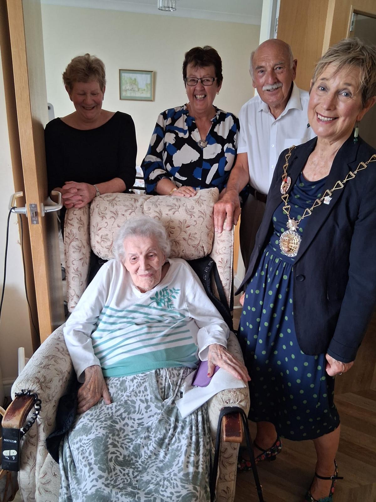 WWII veteran Elsie Vickers is sat in a chair with Cllr Linda Bird standing to her left. Two women and one man are stood behind them.