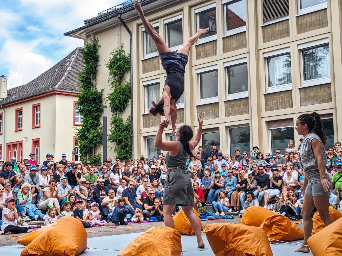 Acrobats perform for a large crowd of people in front of a three story building