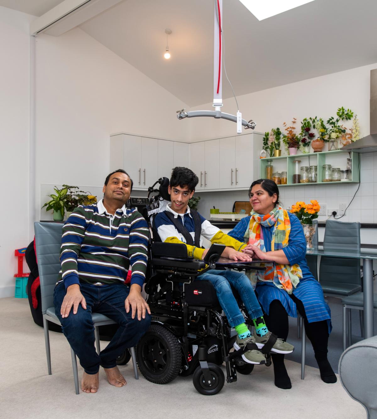 a mother and father with their son who is pictured in a wheelchair in the kitchen of their adapted home.