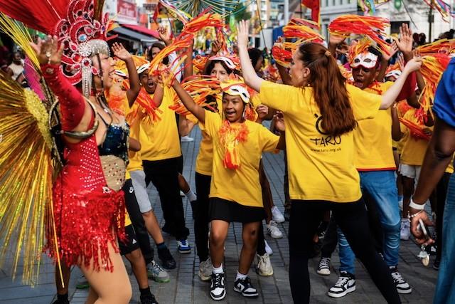 A group of children wearing yellow t shirts and dancing in a carnival parade