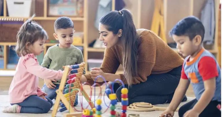 A woman showing a young girl how to use a colourful abacus toy while two boys look on.