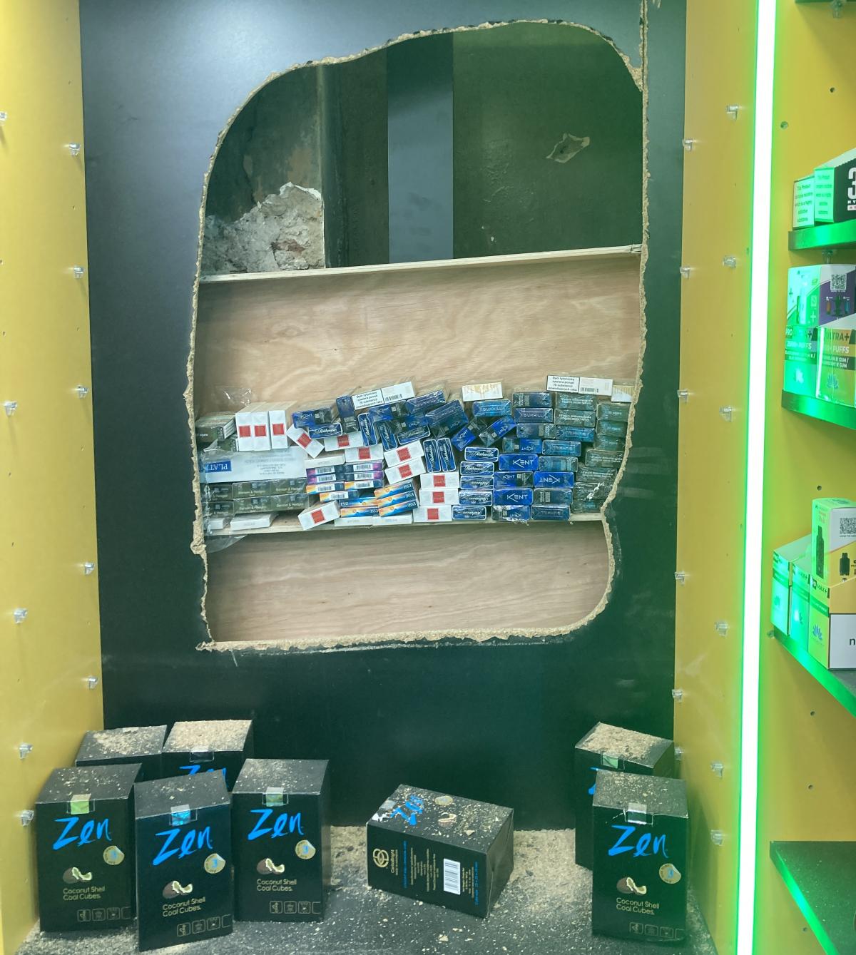 Photo of a hole in a wall revealing hundreds of packets of cigarettes