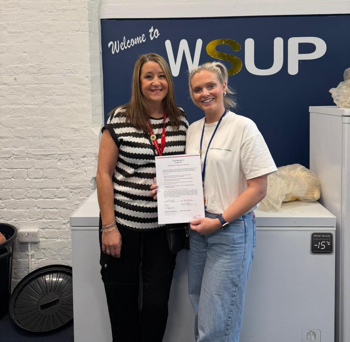 A photo of two people holding the Women's Safety Charter in front of a board which says 'Welcome to WSUP'