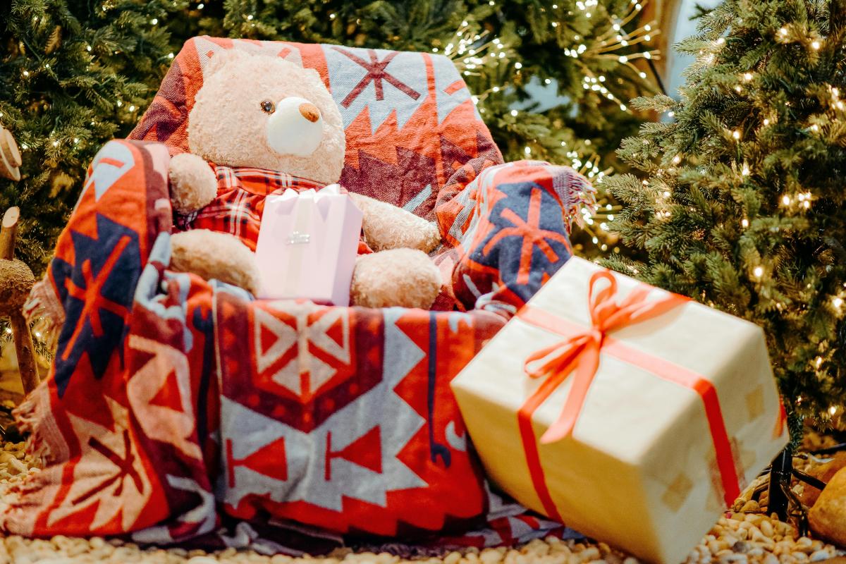 large armchair next to a christmas tree with a teddy on the chair and presents on the floor