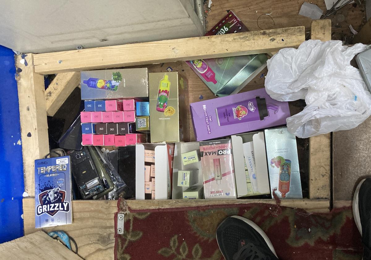 Underneath a floor panel which reveals illegal vape and tobacco products.