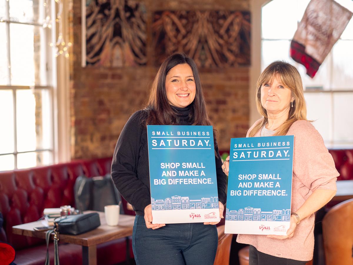 Small Business Saturday - two businesswomen stood smiling to camera, holding Small Business Saturday signs