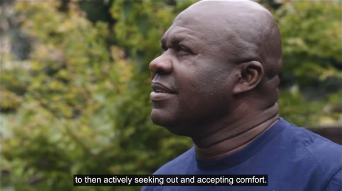 Man looking into the horizon speaking about experience fostering, the background features greenery like in a garden.