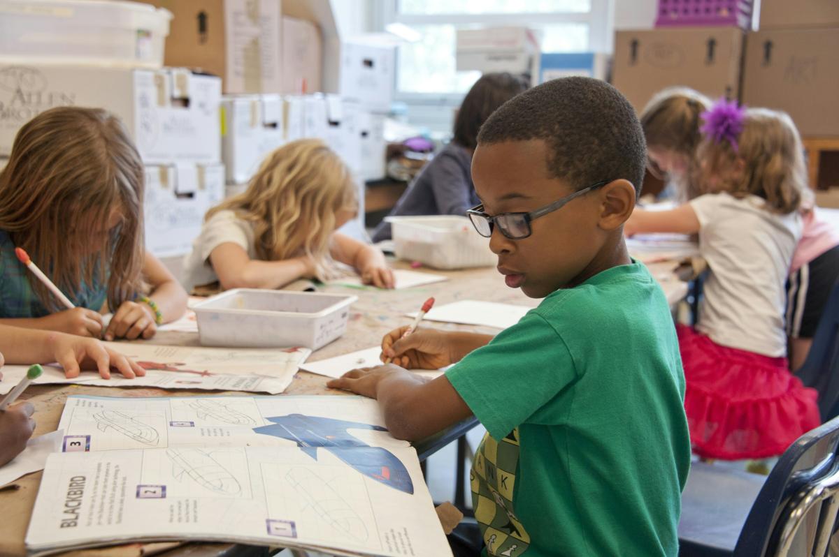 Primary school student doing work at a desk with other children around