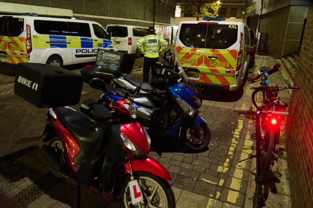 Red and blue illegal mopeds and e-bikes lined up outside a police van