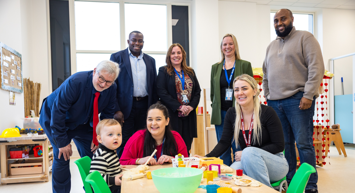 A photo of Clive Efford MP, Leader of the Royal Borough of Greenwich Cllr Anthony Okereke, Cabinet Member for Children and Young People Cllr Adel Khaireh smile with staff and children at More2Kidbrooke nursery in Kidbrooke.
