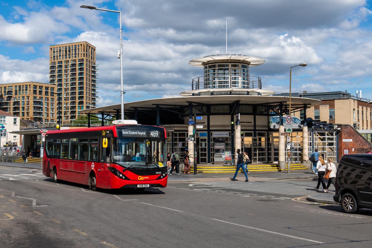 A single-decker red 469 bus outside a train station on a sunny day.